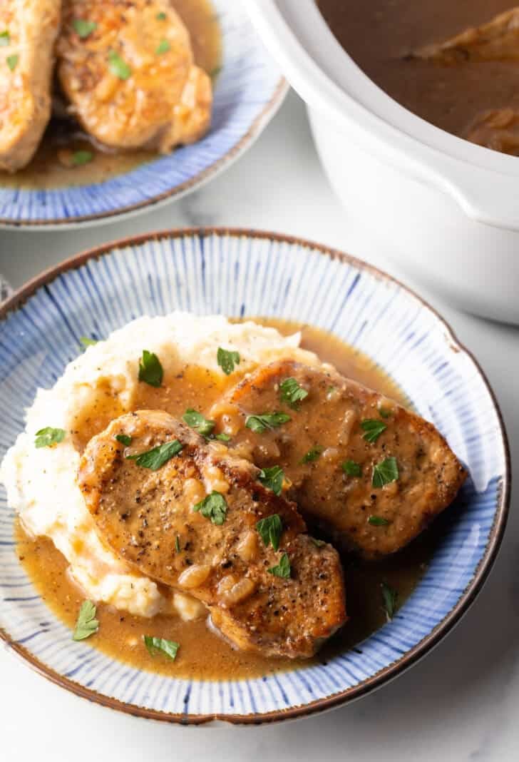 Two boneless pork chops on a plate of mashed potatoes and brown onion gravy.