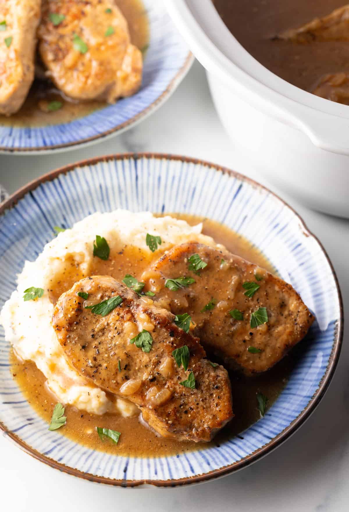 Two boneless pork chops on a plate of mashed potatoes and brown onion gravy.