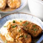 Two boneless pork chops on a plate of mashed potatoes and brown onion gravy.
