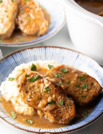 Two boneless pork chops on a plate of mashed potatoes and brown onion gravy.