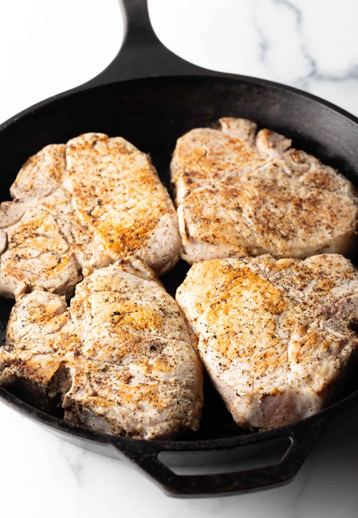 4 bone-in pork chops in a cast iron skillet.