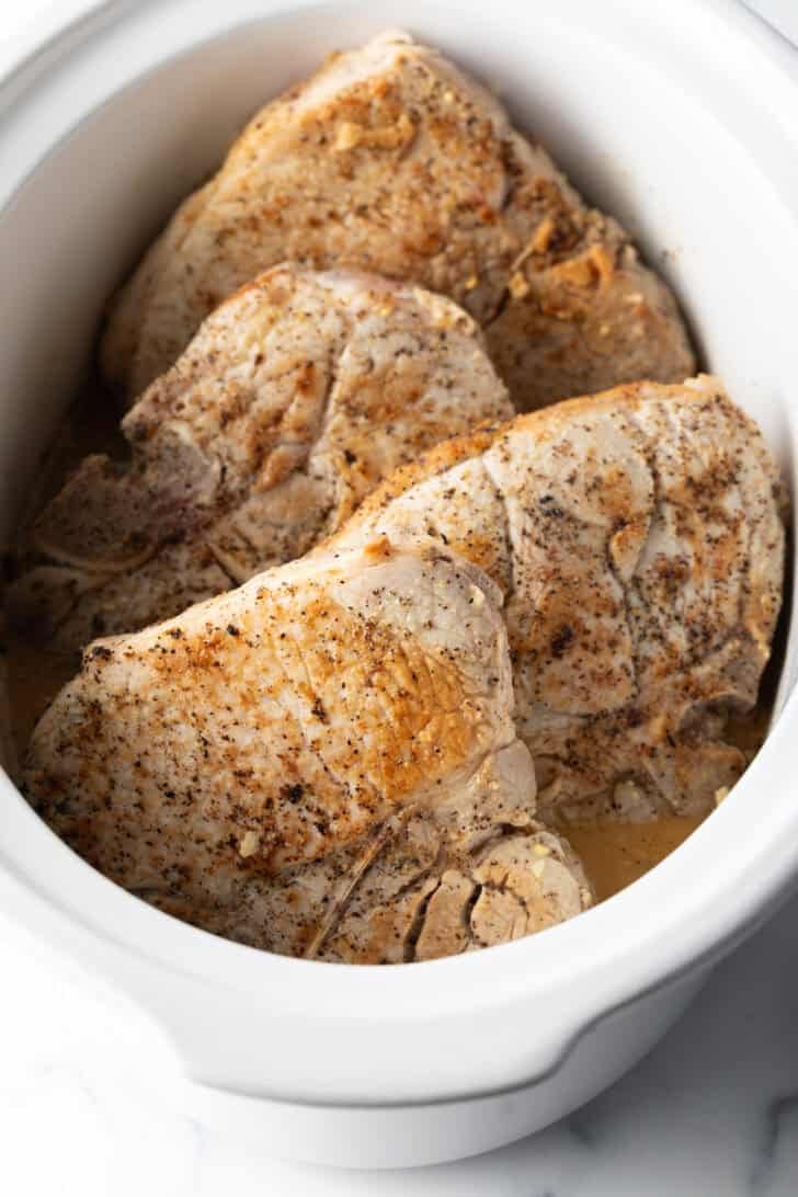 4 bone-in seared pork chops in a white crock pot.