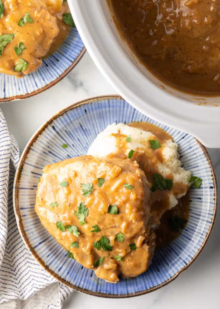 A large bone-in pork chop on a bed of mashed potatoes, topped with onion gravy and chopped parsley.