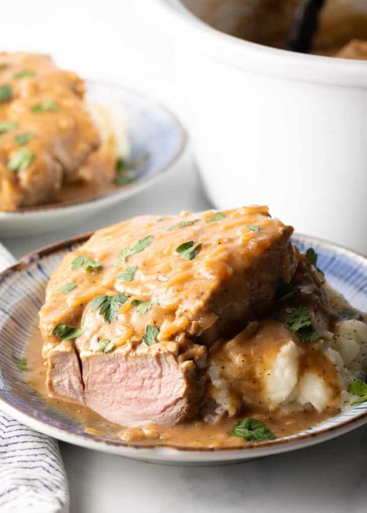 A cooked pork chop covered in brown gravy with a piece cut off the end, showing the moist meat.