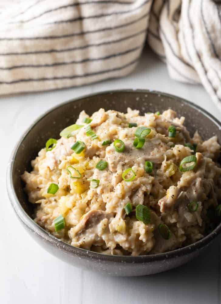Brown rice chicken and rice in a black bowl, topped with chopped scallions.
