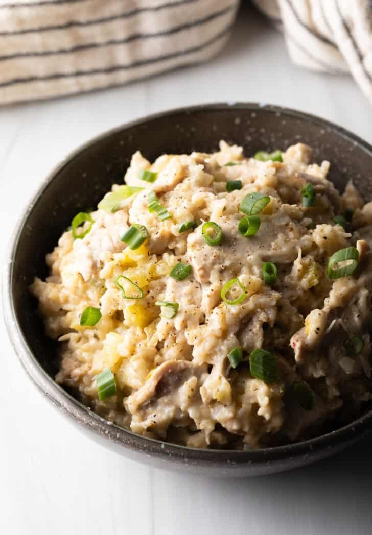 Brown rice chicken and rice in a black bowl, topped with chopped scallions.