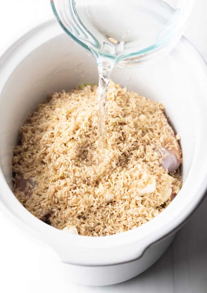 Adding water to a slow cooker with chicken thighs and brown rice.