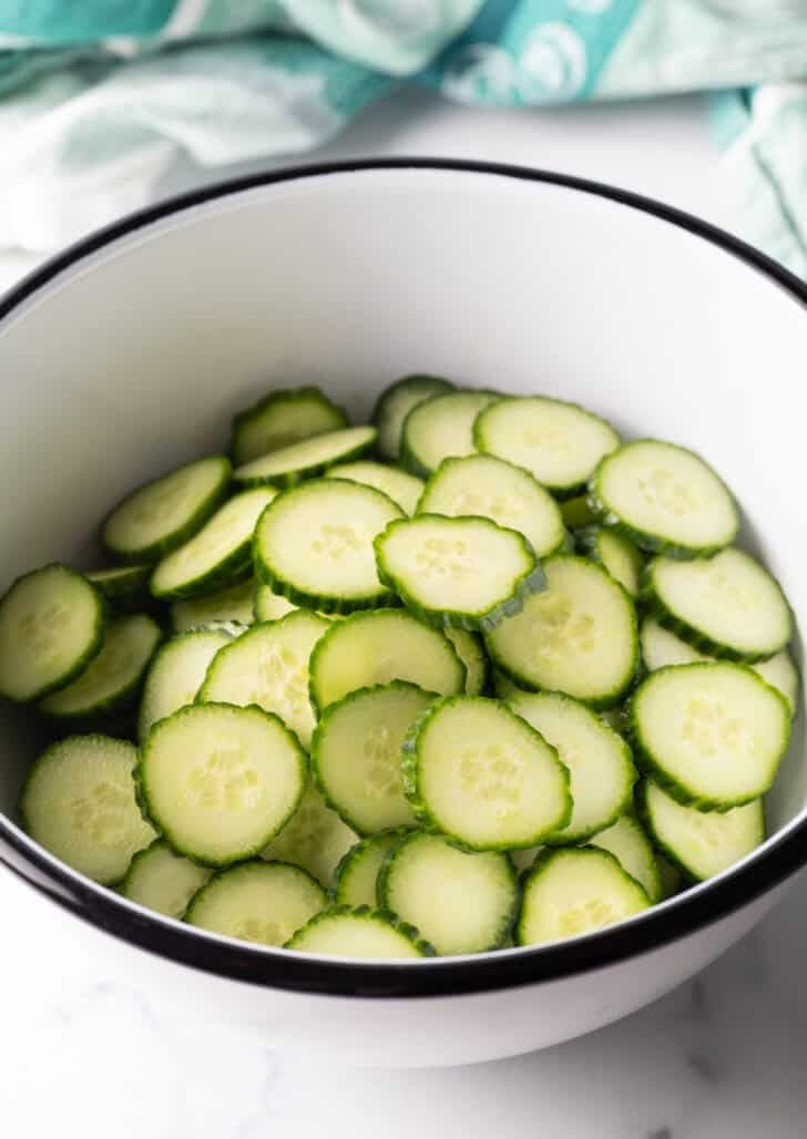 White mixing bowl filled with sliced cucumbers.