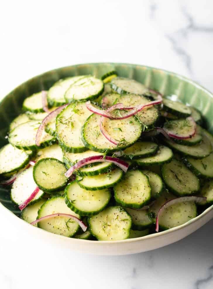 Green plate loaded with sliced cucumbers and red onion salad with dill.