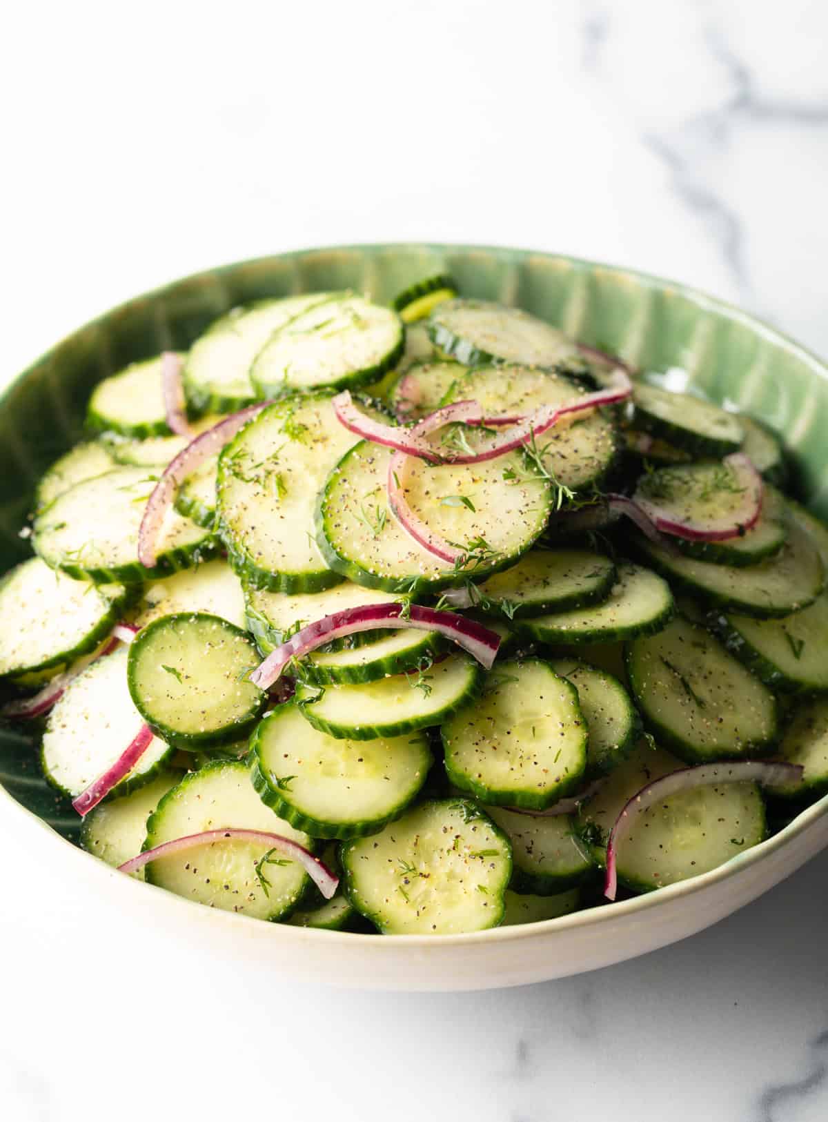 Green plate loaded with sliced cucumbers and red onion salad with dill.