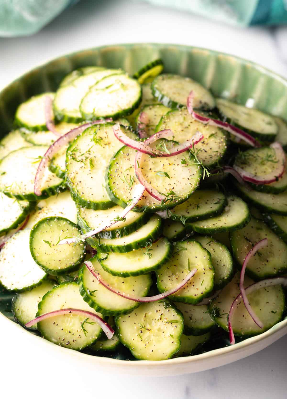 Green plate loaded with sliced cucumbers and red onion salad with dill.