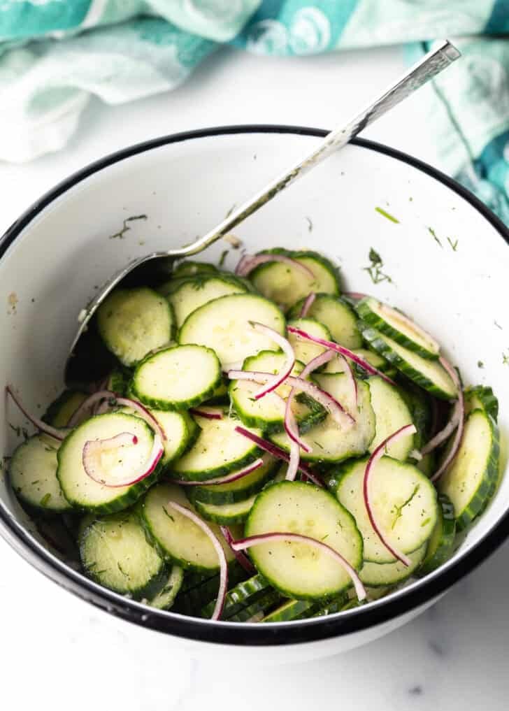 White bowl with sliced cucumbers and red onion slices.