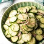 Green plate loaded with sliced cucumbers and red onion salad with dill.