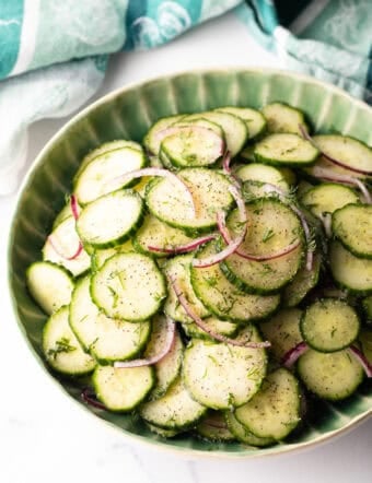 Green plate loaded with sliced cucumbers and red onion salad with dill.