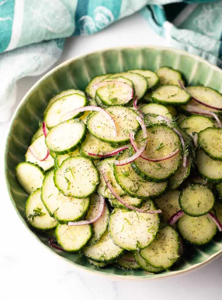 Green plate loaded with sliced cucumbers and red onion salad with dill.