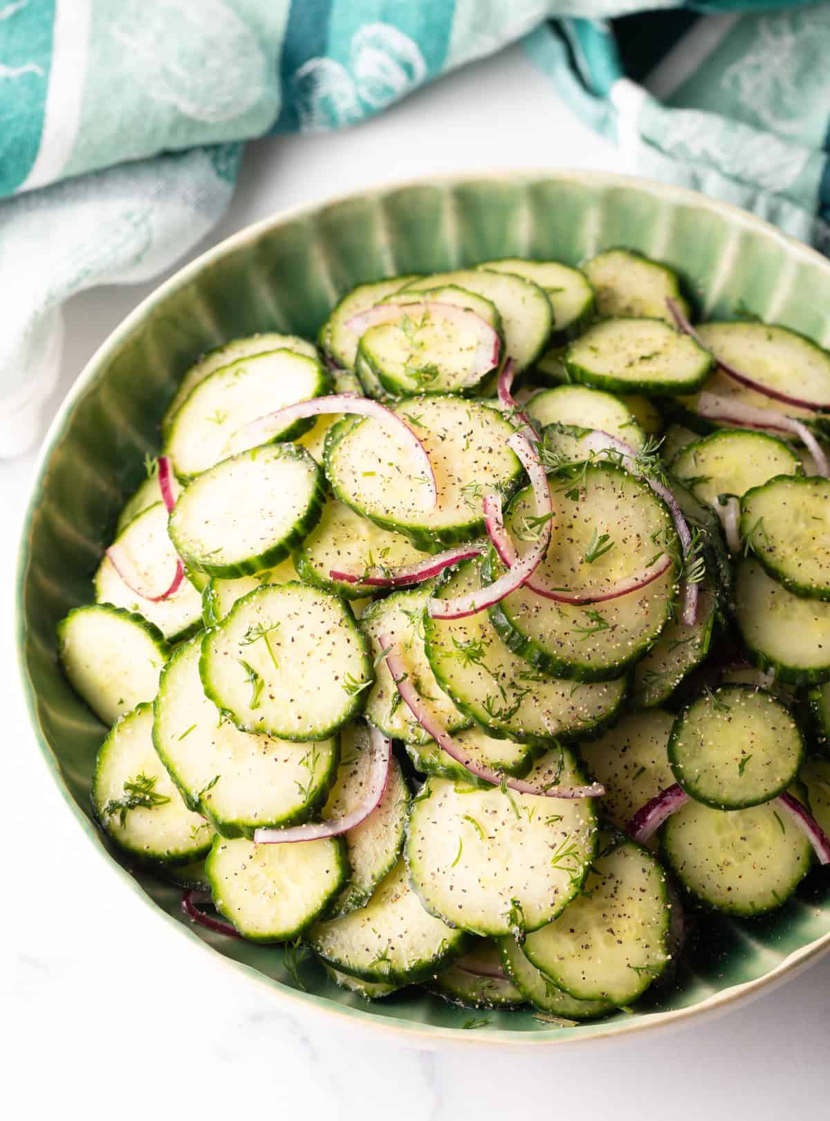 Green plate loaded with sliced cucumbers and red onion salad with dill.