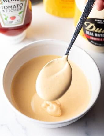 Spoon of burger sauce held over a bowl of sauce.