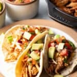 Three chicken tacos with chopped avocado on a plate together.