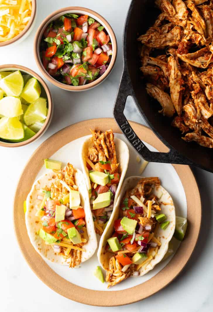 Three chicken tacos with chopped avocado on a plate together.