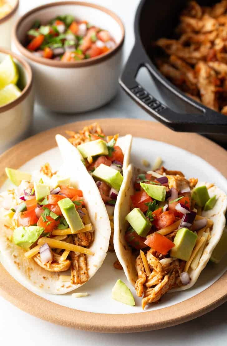 Three chicken tacos with chopped avocado on a plate together.