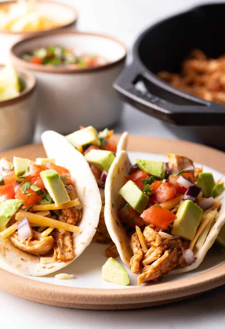 Three chicken tacos with chopped avocado on a plate together.