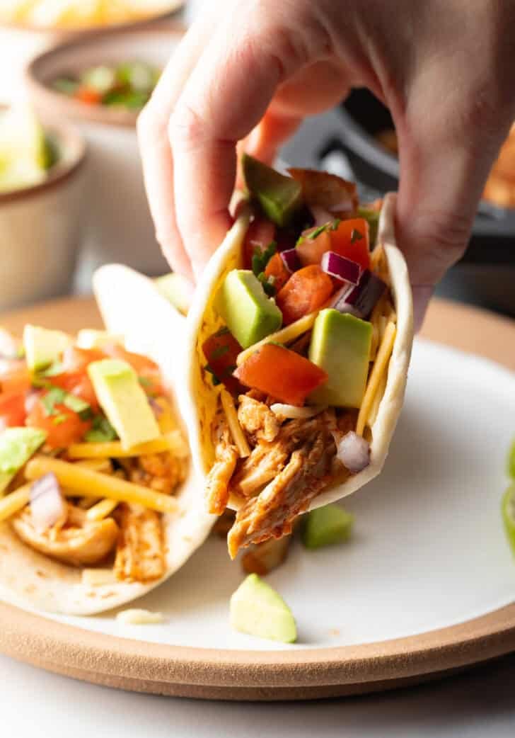 Hand picking up a taco with chicken, salsa, and chopped avocado.