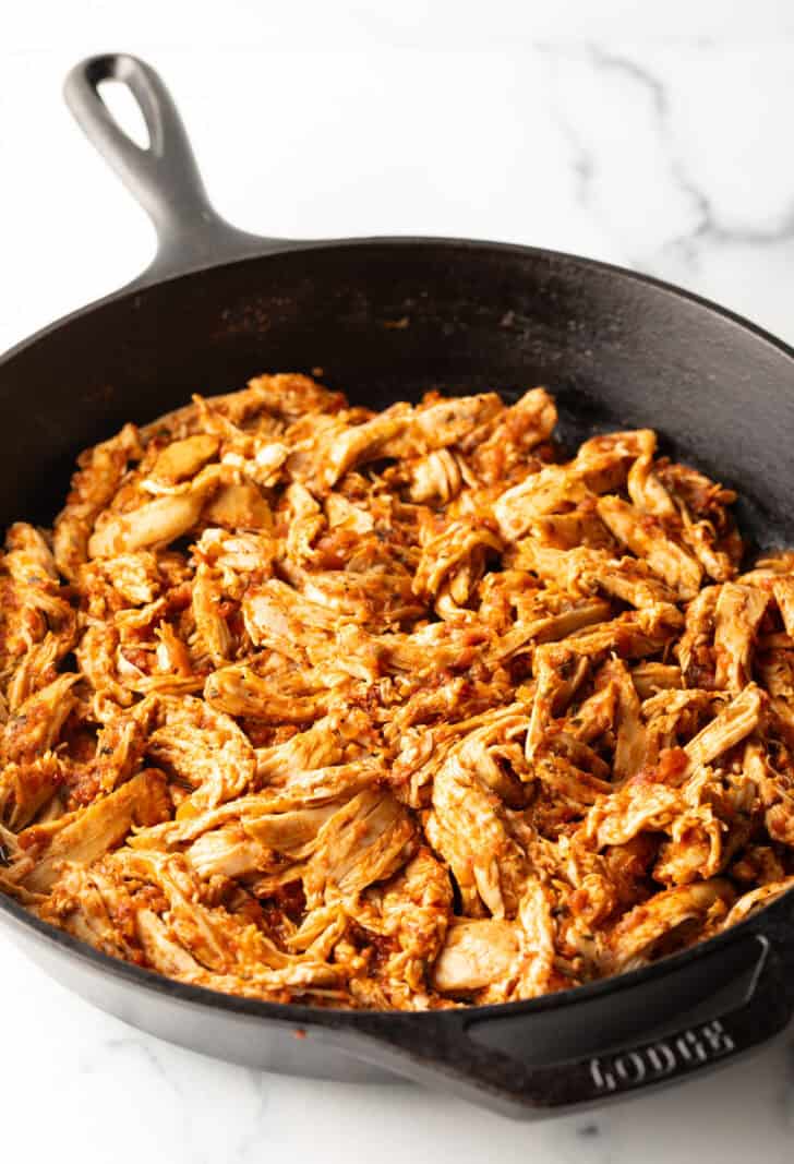 Shredded chicken and tomato sauce in a cast iron skillet.