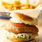 Battered and fried fish sandwich on a bun with coleslaw, tartar sauce, and a slice of tomato.