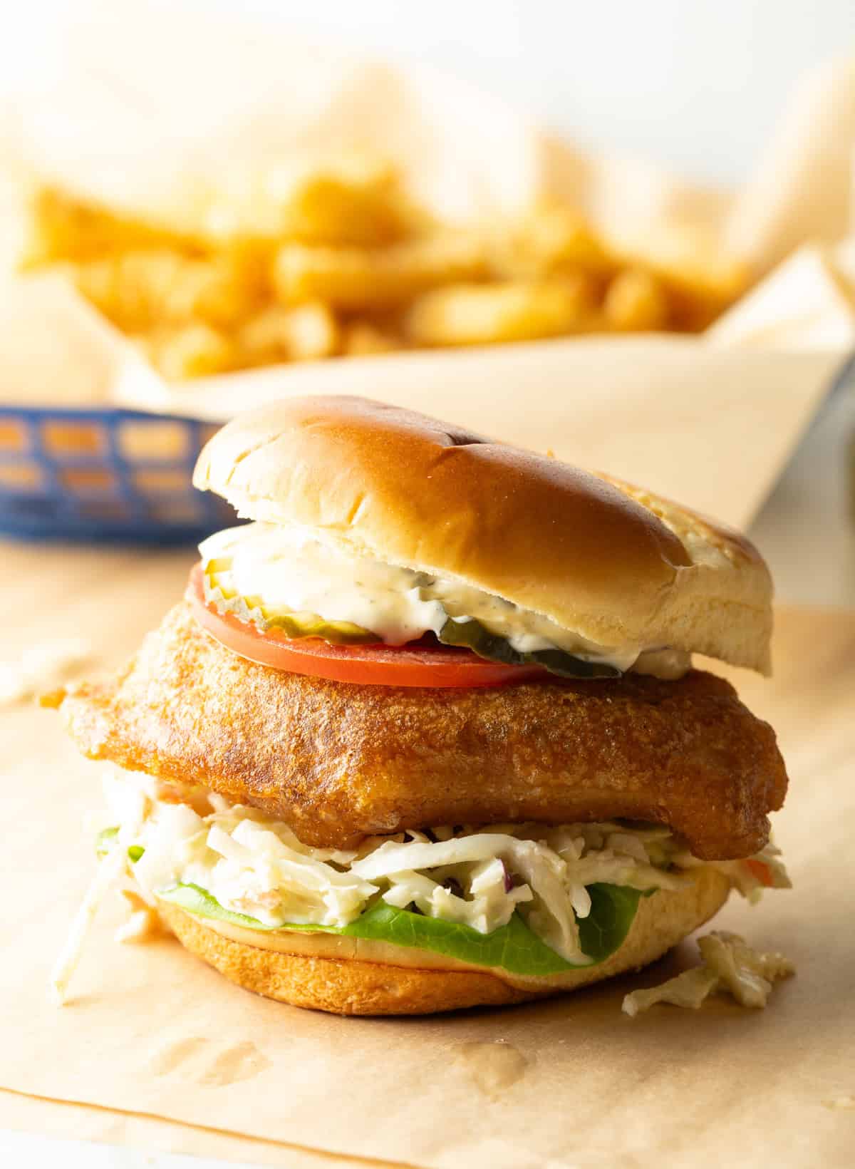Battered and fried fish sandwich on a bun with coleslaw, tartar sauce, and a slice of tomato.