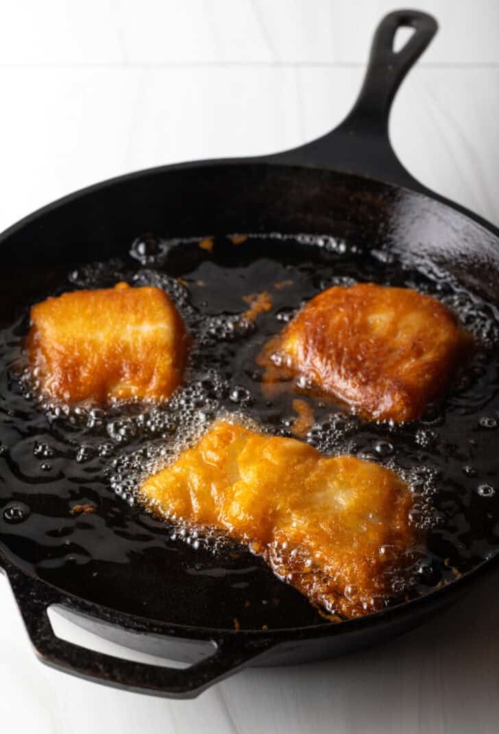 Frying pieces of breaded fish in a cast iron skillet.