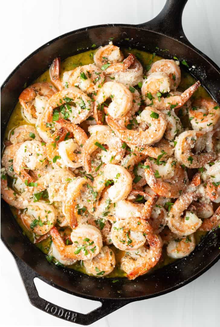 Top down view cooked shrimp garnished with parsley in a black cast iron skillet.