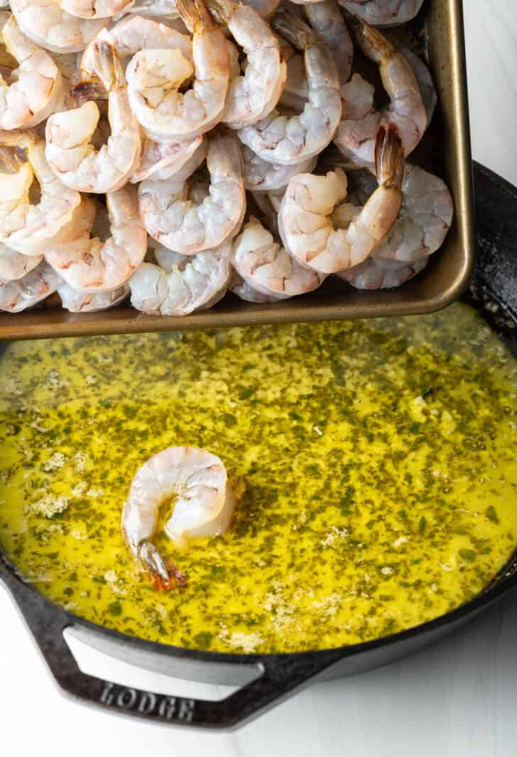 Adding raw shrimp to a skillet with garlic butter and herbs.