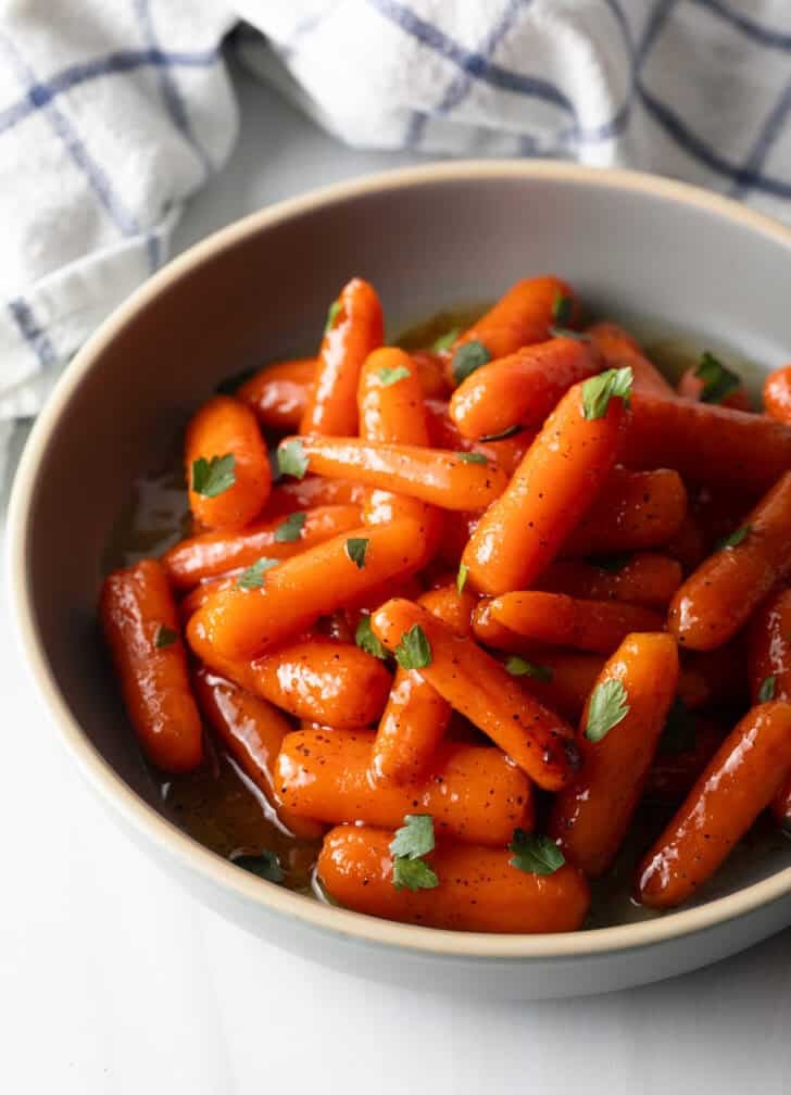Bowl of glazed honey baby carrots sprinkled with chopped parsley.