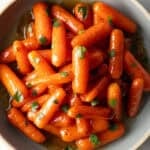 Top down bowl of glazed honey baby carrots sprinkled with chopped parsley.