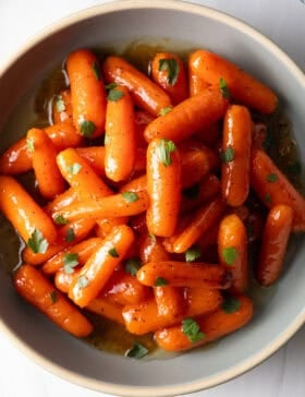 Top down bowl of glazed honey baby carrots sprinkled with chopped parsley.