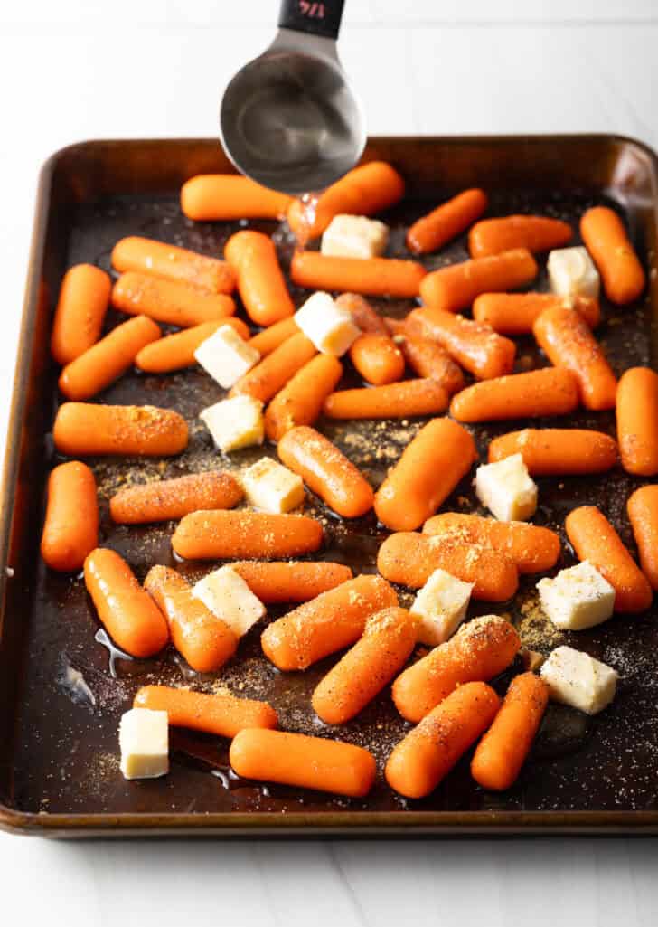 Baking sheet with baby carrots and cubes of butter.