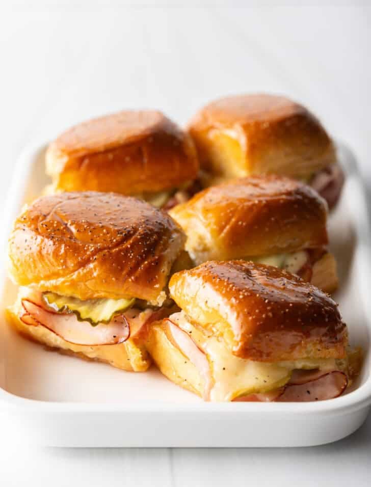 5 King's Hawaiian ham and cheese sliders on a white rectangle plate.