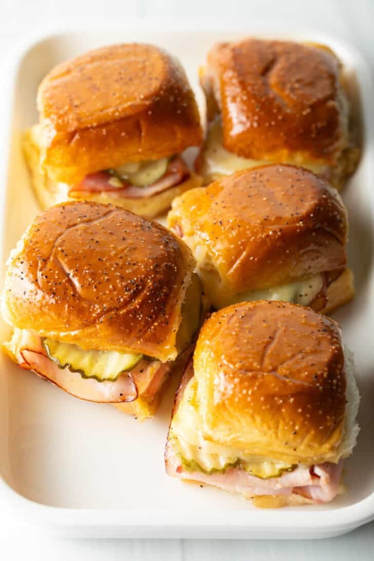 5 King's Hawaiian ham and cheese sliders on a white rectangle plate.