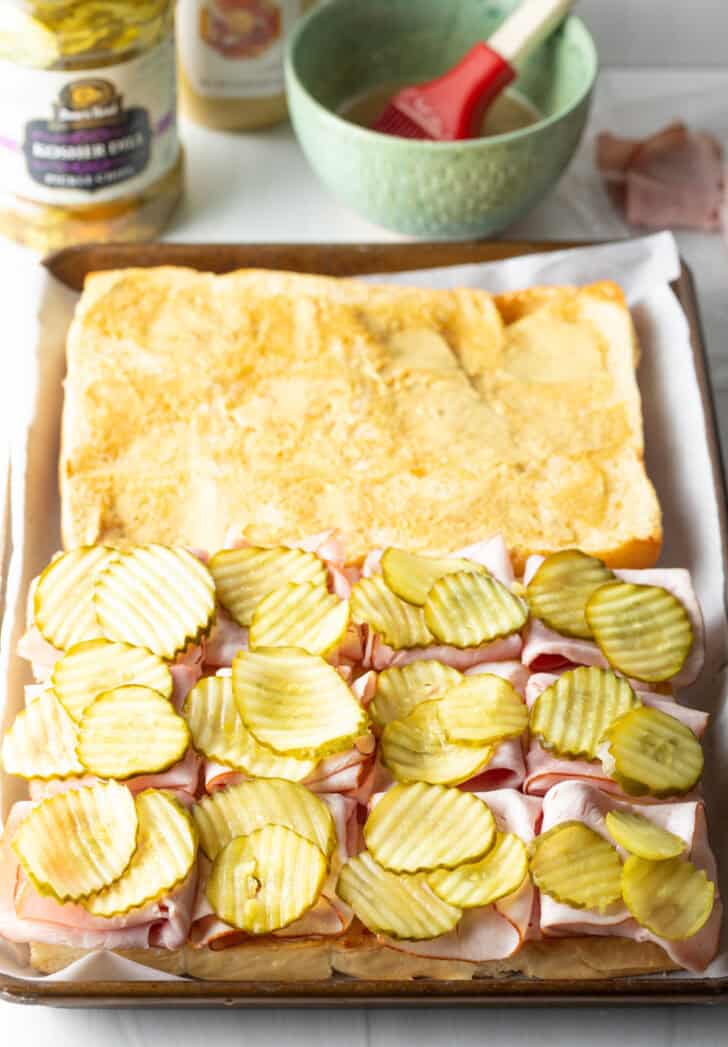 Assembling the King's Hawaiian rolls with pickles and squares of cheese on top of the ham.