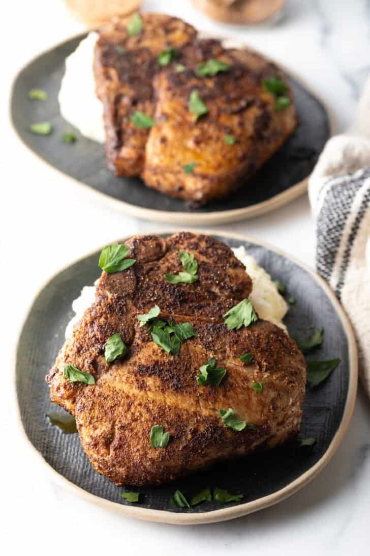 Browned seasoned bone-in pork chop on a plate, garnished with chopped parsley.