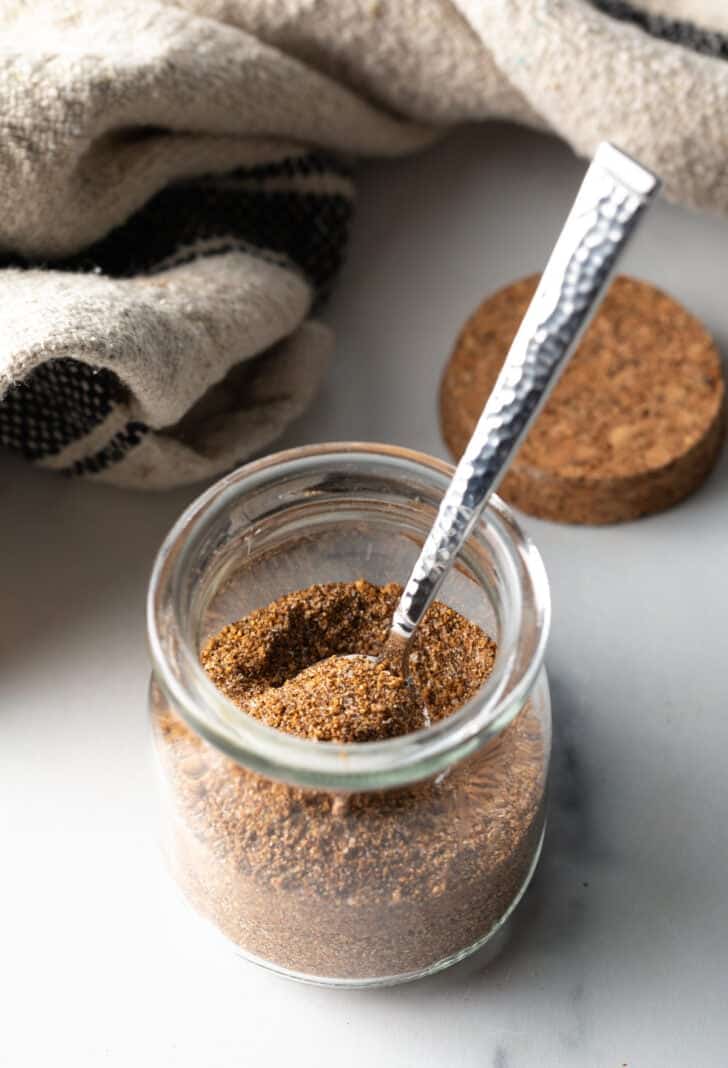 Small glass jar with pork chop seasoning and a metal spoon.