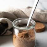 Small glass jar with pork chop seasoning and a metal spoon.
