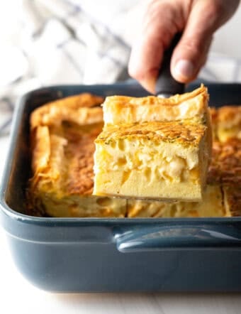 Hand removing a square of egg casserole with a spatula from a square baking dish.