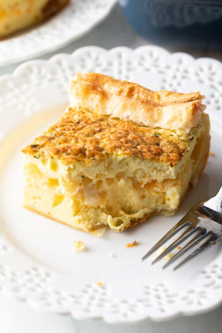 Square of egg casserole on a white plate with a fork.