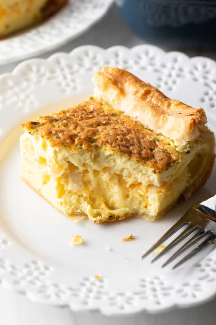 Square of egg casserole on a white plate with a fork.