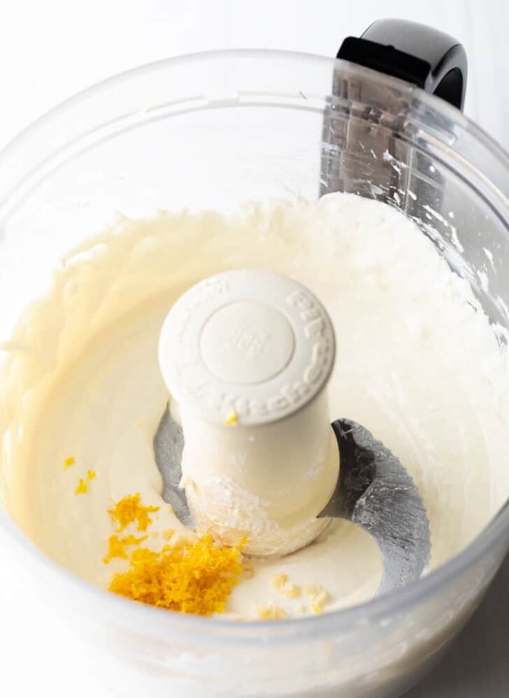 Adding lemon zest to creamy cheese and sour cream in a food processor.