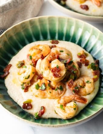 Green bowl with cheesy grits and topped with Cajun shrimp and chopped bacon.