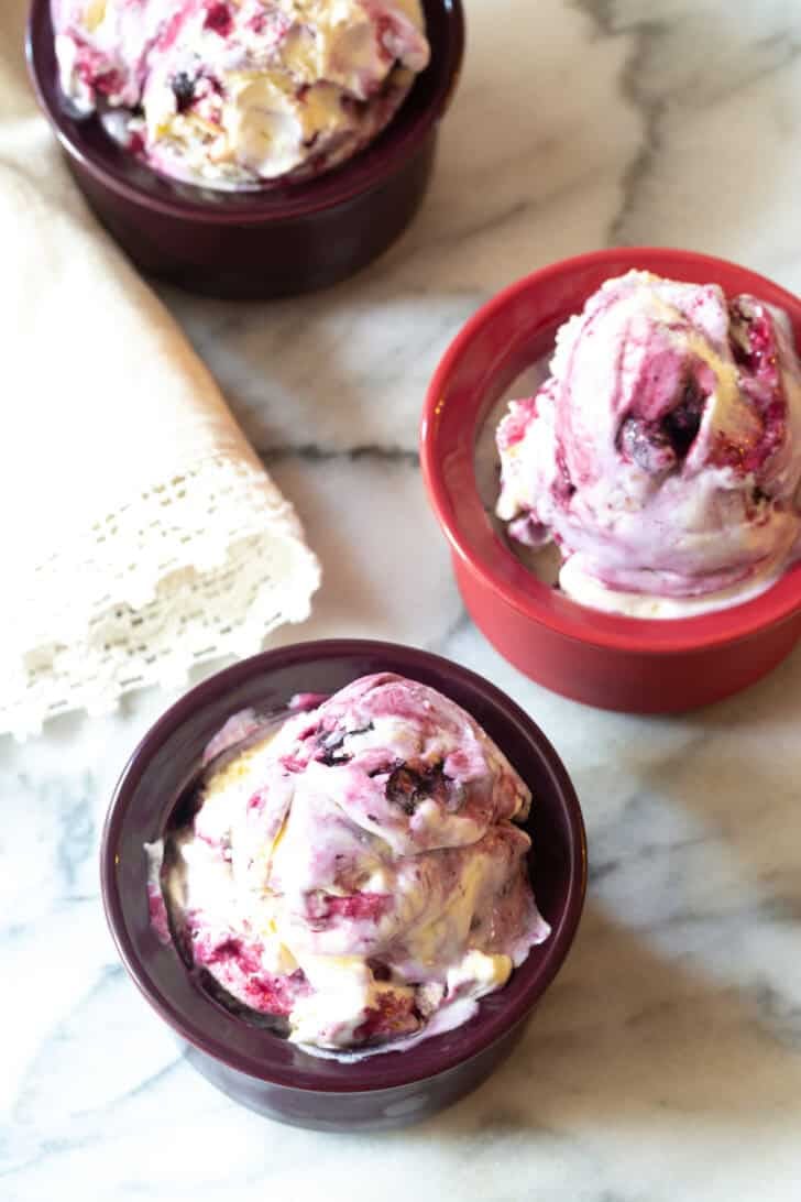 Top down view three bowls of blueberry ice cream with spoons.