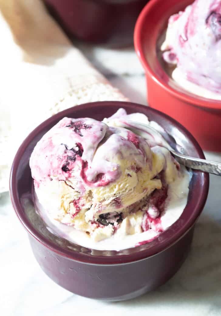 Dark bowl with blueberry pie ice cream. A spoon is taking a scoop from the bowl.