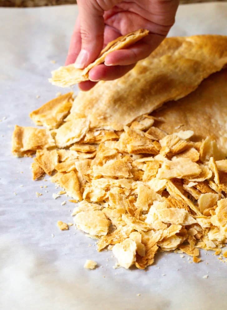Hand cracking a piece of baked pie crust into small pieces.